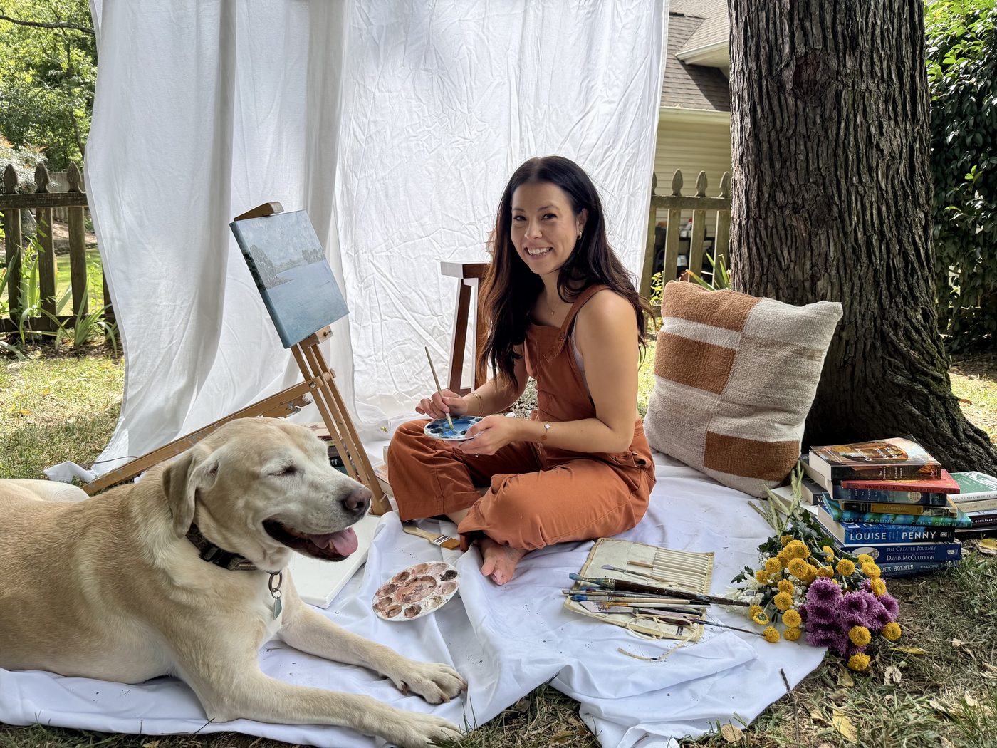Tara Venturini-Bush of Solaria Studio painting at an easel outdoors with her dog beside her